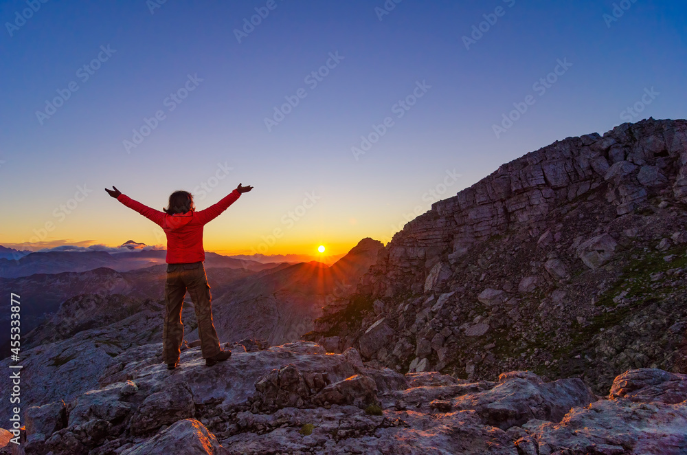 Happy hiker girl meets sunrise with raised arms high in the mountains. ©Adobestock